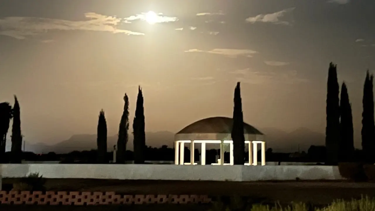 A domed pavilion glowing under a bright moon, cypress silhouettes around it