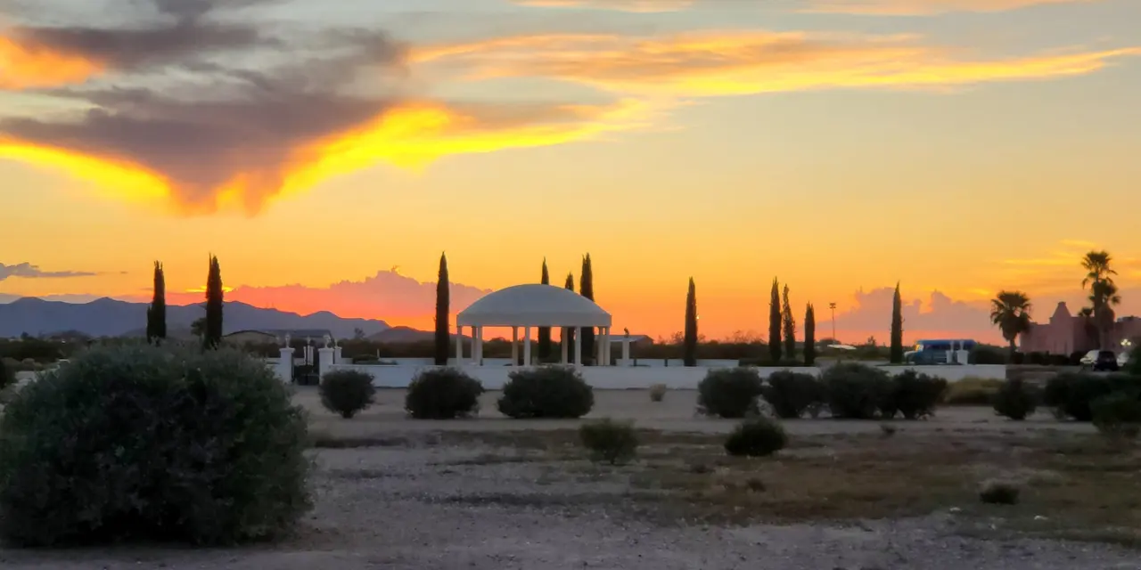 Fiery sunset clouds over the desert, cypress trees and a domed pavilion